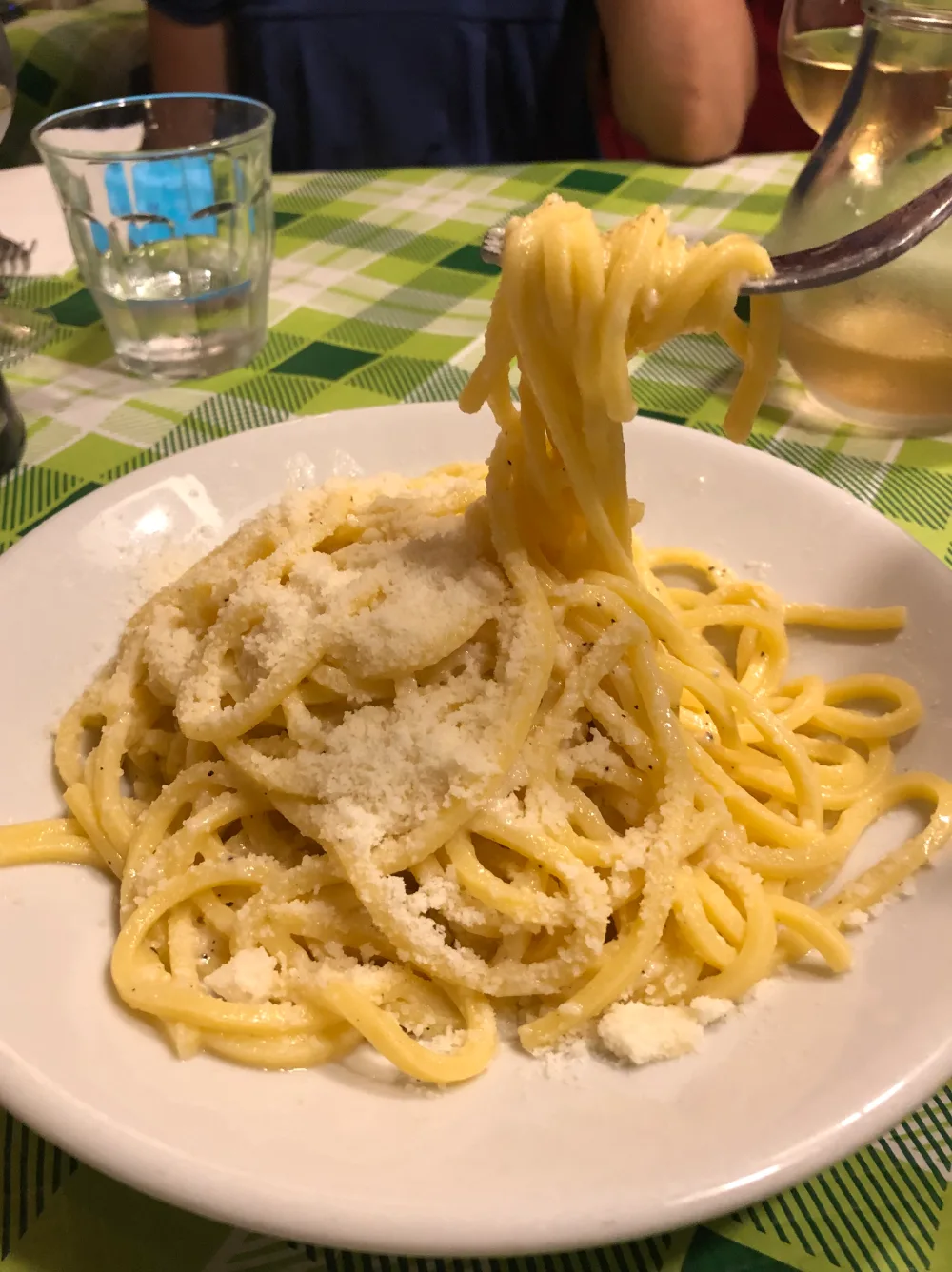 A plate of cacio e pepe pasta being lifted with a fork at a trattoria in Rome