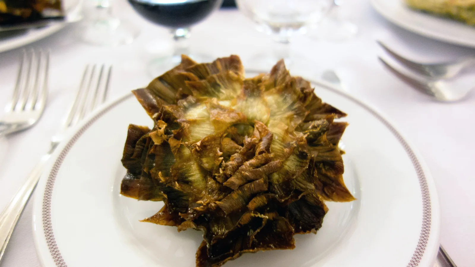 A whole Jewish-style fried artichoke served on a white plate