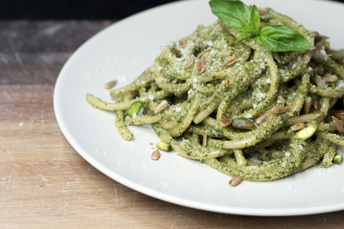 Pasta tossed in green basil pesto with a basil sprig on a white plate