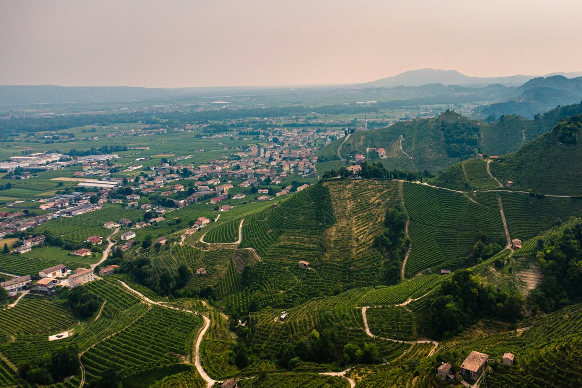 Aerial view of steep green hills and a small town, the landscape of Prosecco hills tours
