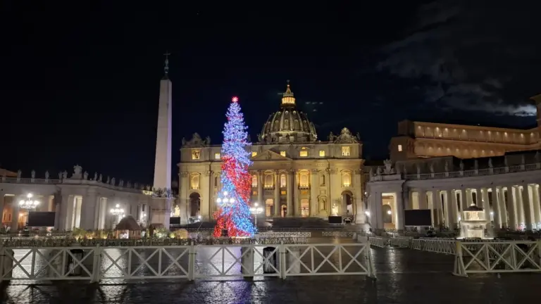 St. Peter's Square at night with a lit Christmas tree beside the obelisk and the basilica behind