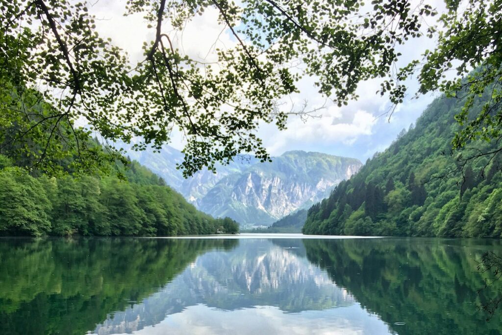 A calm lake reflecting forested mountains at Levico Terme in Valsugana